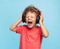 Curly boy in headphones screaming with eyes closed on blue background.